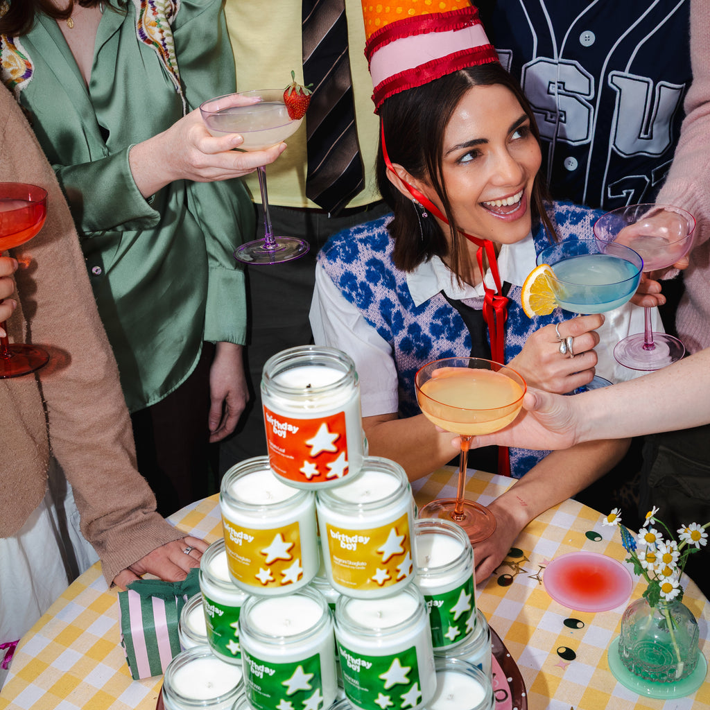 Woman in a party hat surrounded by colorful candles and drinks at a festive gathering.