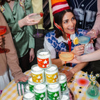 Woman in a party hat surrounded by colorful candles and drinks at a festive gathering.